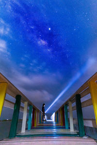 Man holding illuminated flashlight while standing on wood against sky at night