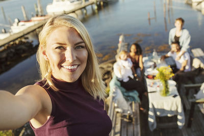 Portrait of smiling young woman with friends in background at jetty