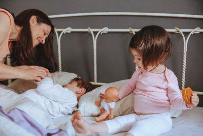 Cheerful mother playing with son and daughter while lying on bed at home