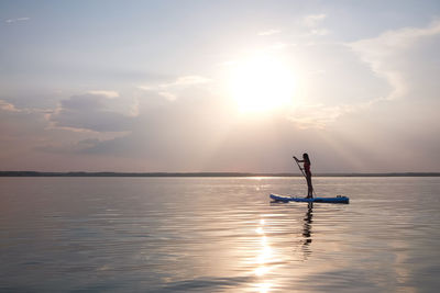 Man fishing in sea against sky during sunset