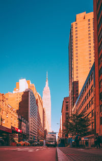 Low angle view of road amidst buildings against clear blue sky