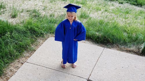 Girl in graduation gown standing against plants