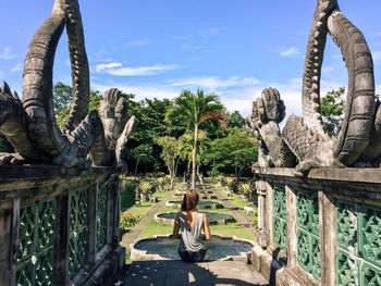 Rear view of woman sitting on steps amidst statues in park