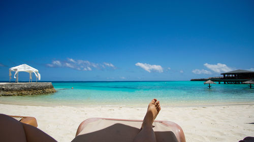 Low section of woman relaxing on beach against sky