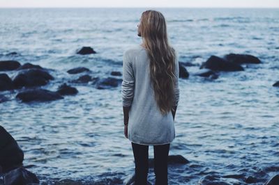 Rear view of friends standing on rock in front of sea