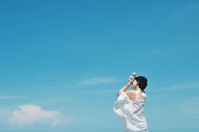 Low angle view of woman photographing against blue sky