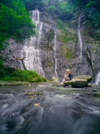 Rear view of man sitting against waterfall