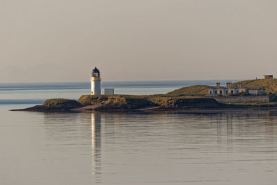 Lighthouse amidst sea and buildings against sky