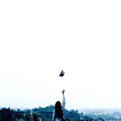 Rear view of woman throwing hat on mountain against clear sky