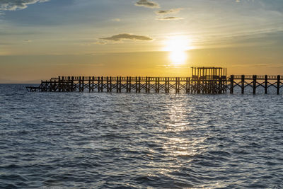 Silhouette wooden posts in sea against sky during sunset