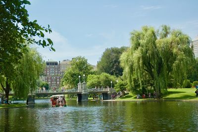 People by lake in city against sky