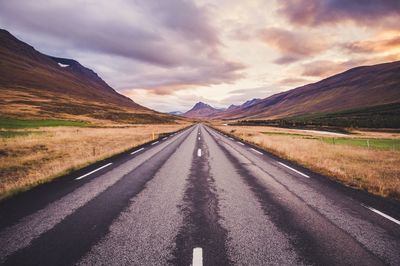 Road passing through landscape against dramatic sky