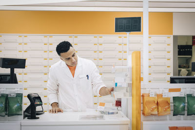 Confident pharmacist examining medicines at checkout in medical store