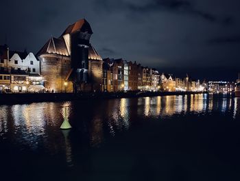 Illuminated buildings by river against sky at night