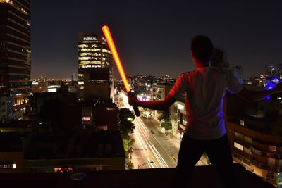 Rear view of man standing by illuminated buildings in city at night