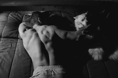 Rear view of shirtless man sleeping with dog on bed at home