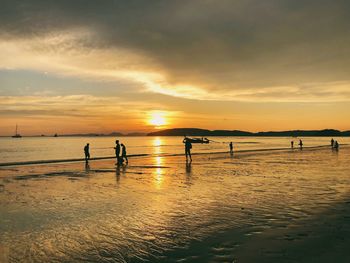 Silhouette people standing on beach against sky during sunset