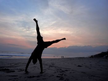 Silhouette woman with arms raised on beach against sky during sunset