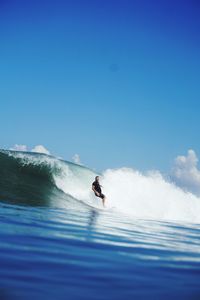 Person surfing in sea against clear blue sky