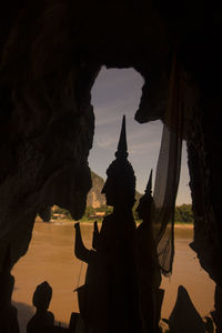 Silhouette buddha statues at pak ou caves by river during sunset