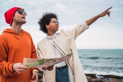 Friends looking away while standing by sea against sky