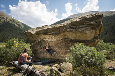 Woman looking at female friend bouldering on rock