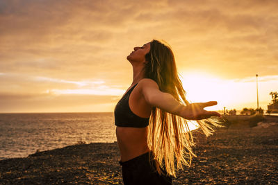 Woman standing by sea against sky during sunset