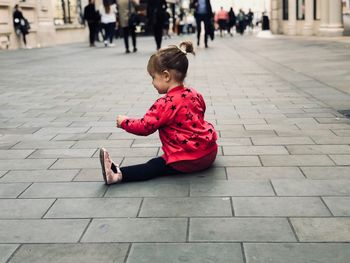 Girl sitting on footpath in city