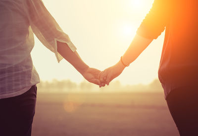 Midsection of man holding hands against sky during sunset