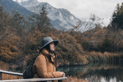 Young woman standing on wooden deck by lake in autumn