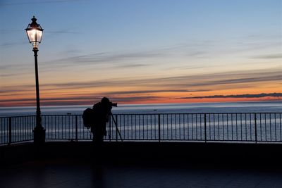 Silhouette man standing by railing against sea during sunset