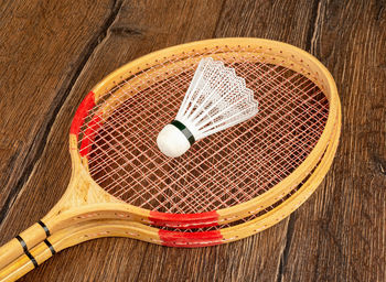 Wooden rackets and a plastic shuttlecock for playing badminton on a wooden background.