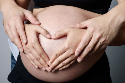 Midsection of husband making heart shape on pregnant woman stomach