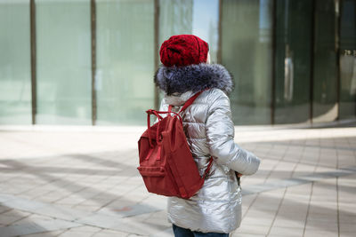 Happy young woman in winter jacket with backpack near building