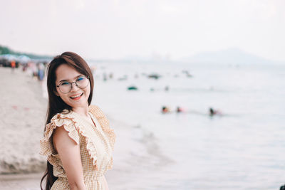 Portrait of beautiful woman wearing sunglasses gesturing while standing at beach