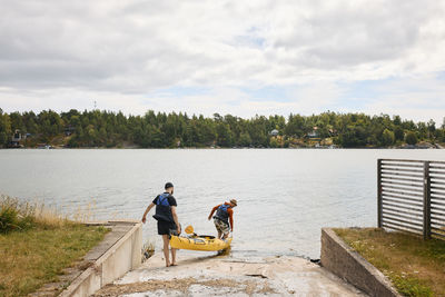 Rear view of men carrying kayak at coast