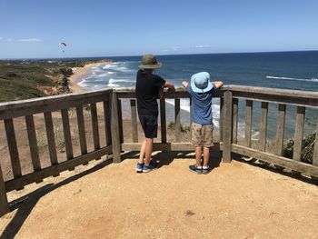 Rear view of men standing by railing against sea