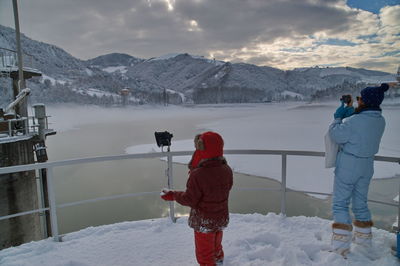 Rear view of man photographing on snowcapped mountains against sky