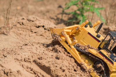 Small plastic toy digger working on sand quarry, construction concept