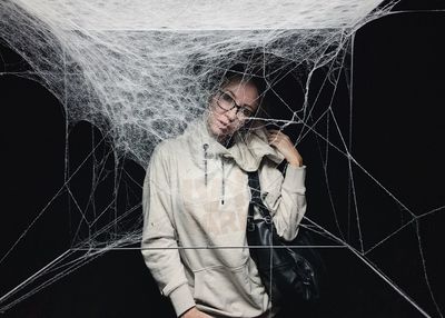 Digital composite image of young woman standing amidst web against black background
