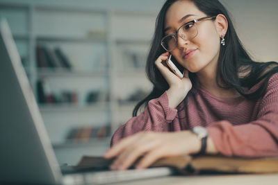 Portrait of young woman using phone while sitting on table