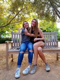 Smiling sisters embracing while sitting on bench in park