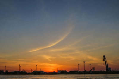 Silhouette of factory against sky during sunset