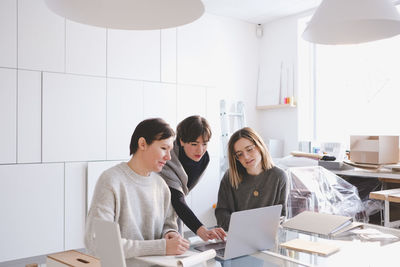 Female fashion designers discussing over laptop at desk in workshop