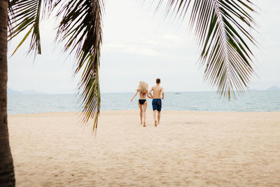 Rear view of couple running on beach against sky