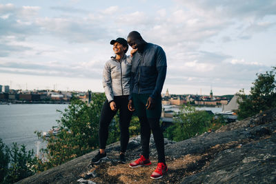 Full length of happy male and female athlete standing on hill against sky