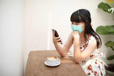 Woman wearing mask using mobile phone at table