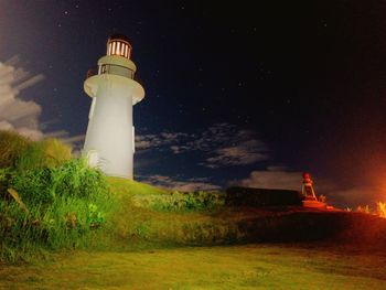 Lighthouse on field by building against sky at night