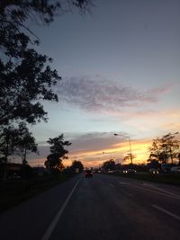 Road by trees against sky during sunset