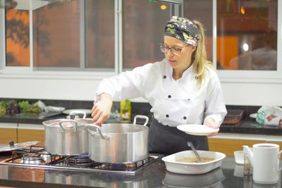 Young female chef cooking food while standing in commercial kitchen